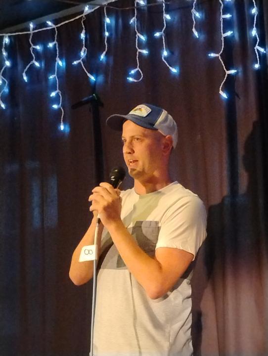 Jason Howell performing stand-up comedy under string lights.